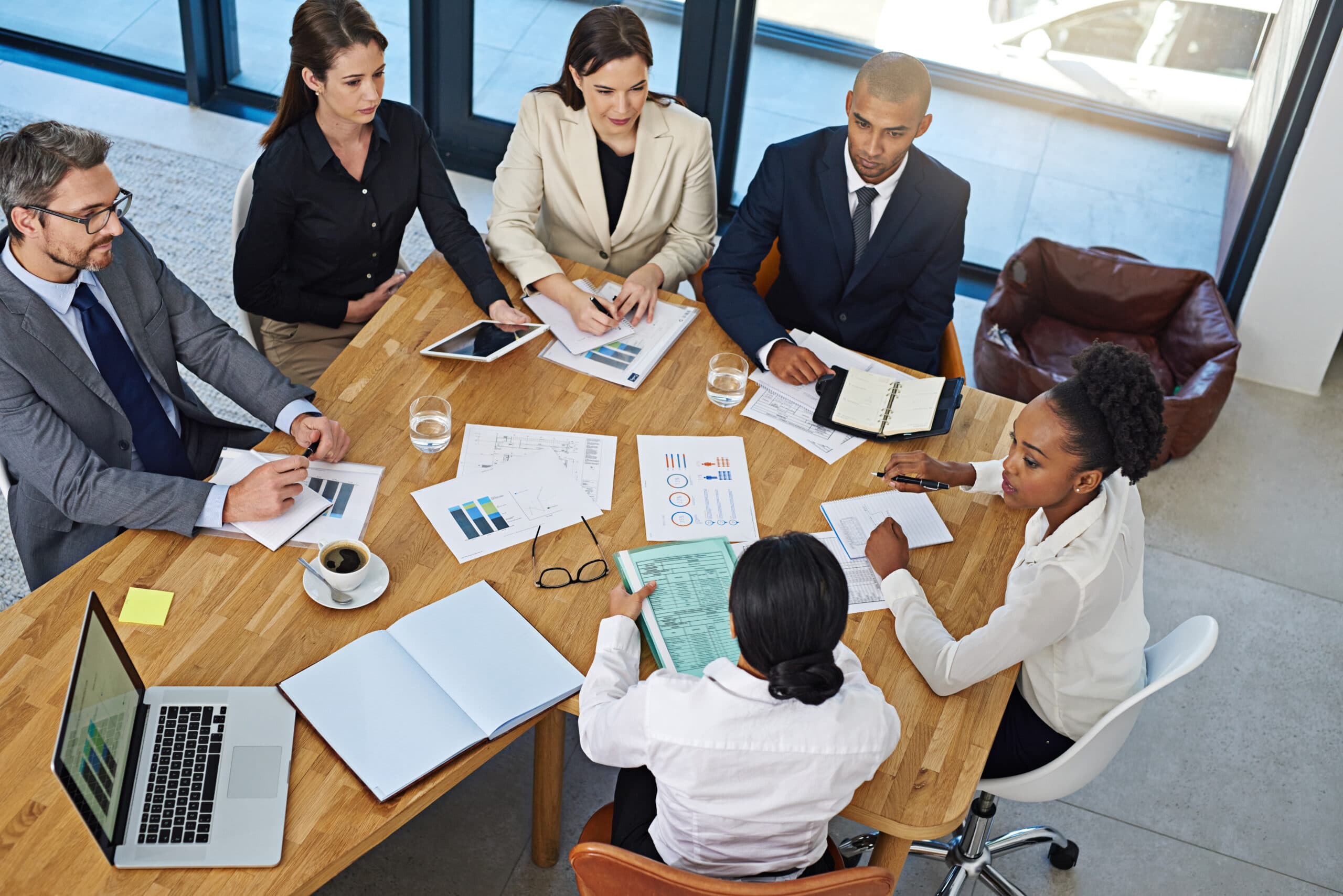 Overhead view of a team meeting around a table covered with charts and reports